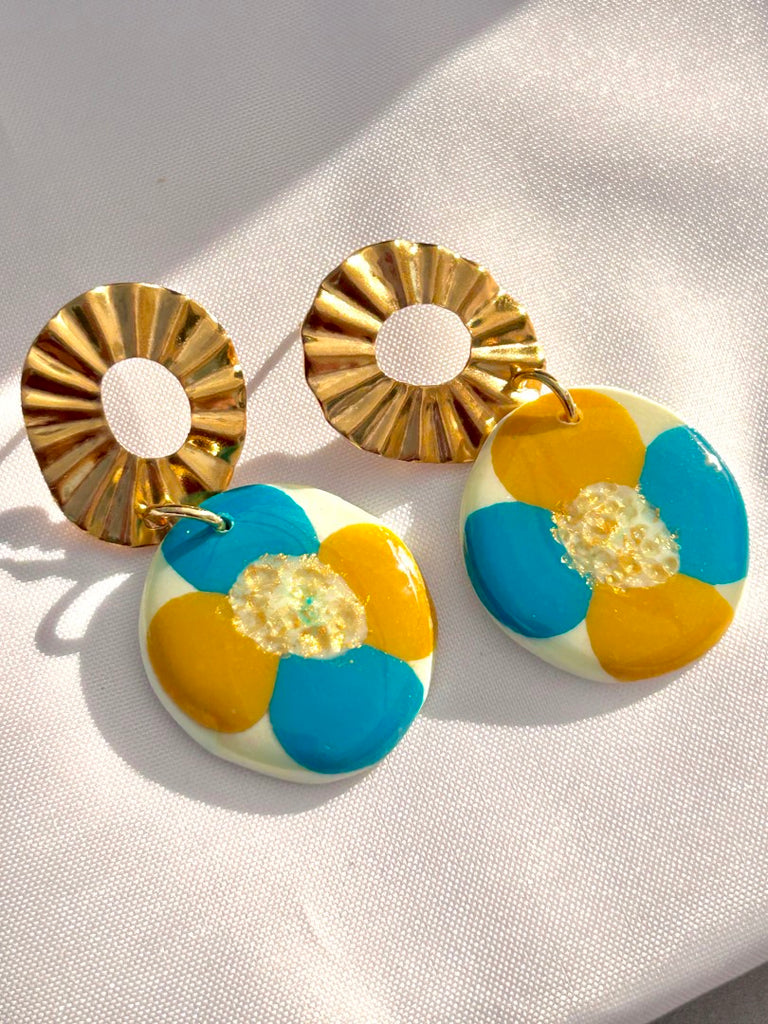 polymer clay floral earrings with large golden sunburst studs, featuring blue and orange petals.