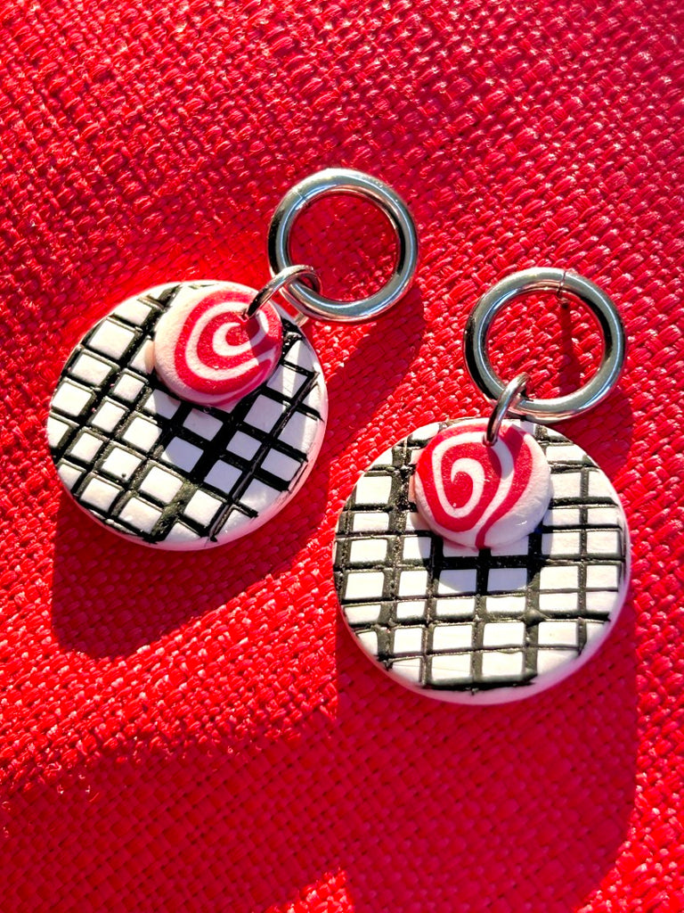 Handmade polymer clay earrings with black and white grid pattern and red swirl design, accented with silver hoops