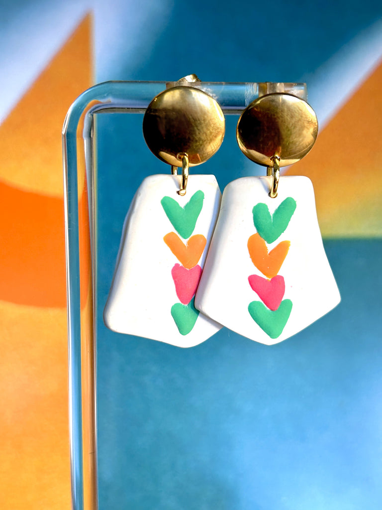 Stacked colourful hearts on a white polymer clay charm earrings with golden hardware