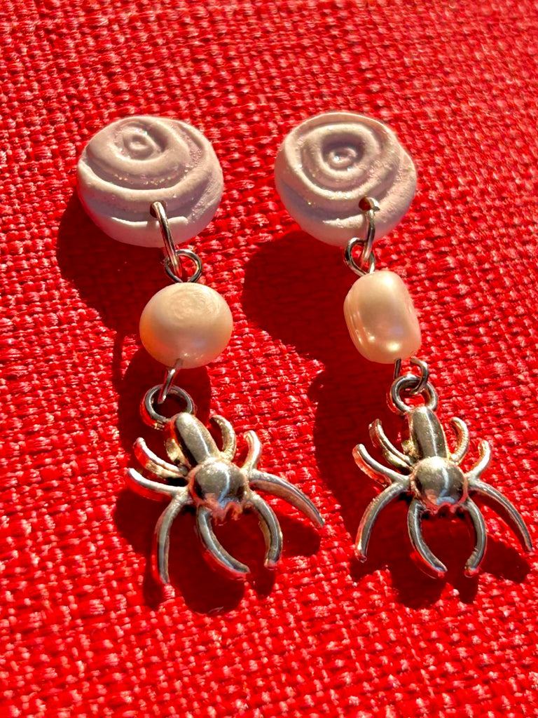 polymer clay earrings with white rose studs, freshwater pearls, and silver spider charms on a red background