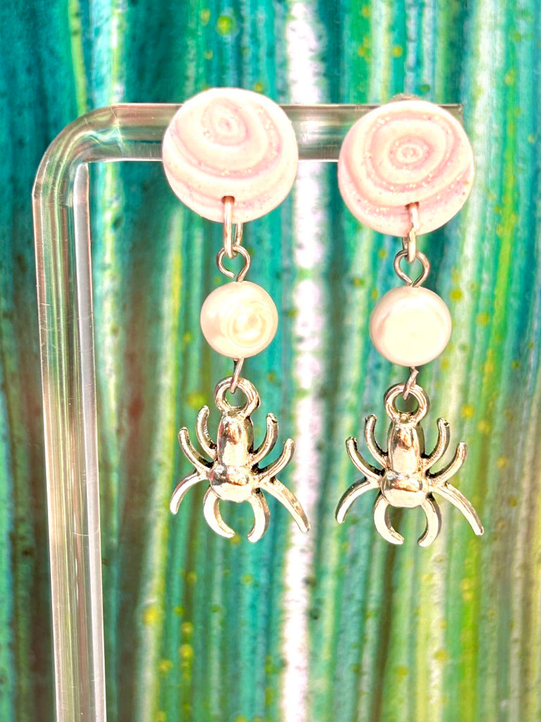 polymer clay earrings with white rose studs, freshwater pearls, and silver spider charms on a red background