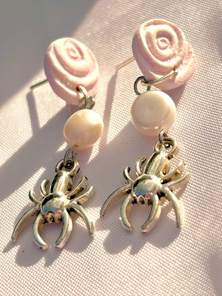 polymer clay earrings with white rose studs, freshwater pearls, and silver spider charms on a red background