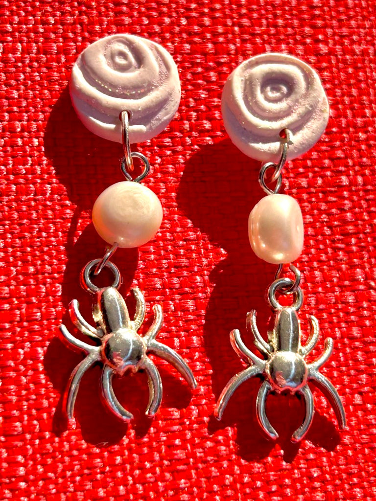 polymer clay earrings with white rose studs, freshwater pearls, and silver spider charms on a red background